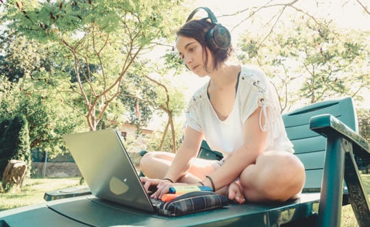 college student outdoors with a laptop and headphones